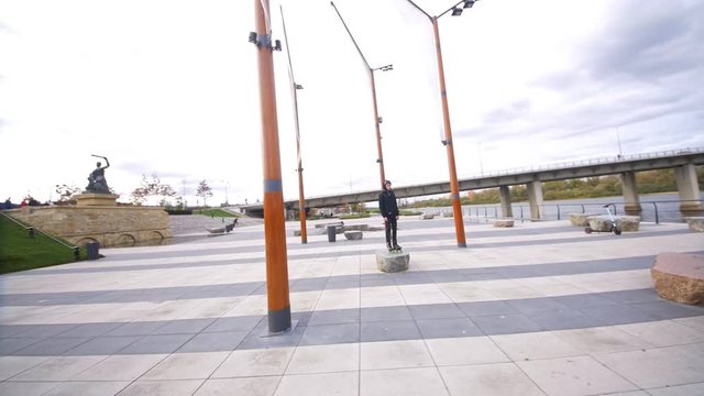 Camera fly around skater staying on stone at promenade in slow motion