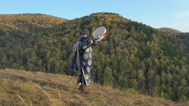 The forest shaman knocks on a tambourine and dances a ritual dance.