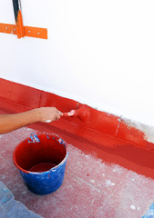 Construction worker waterproofing the terrace of a building with red acrylic rubber paint to solve...