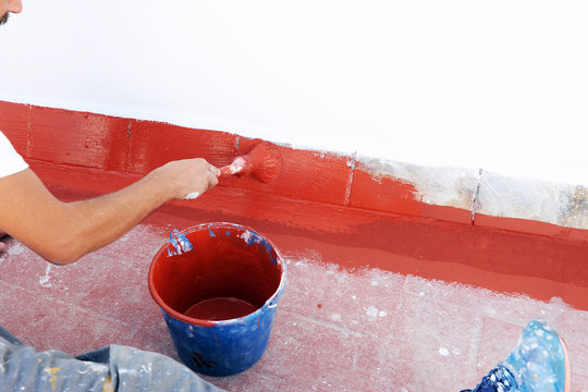 Trabajador de la construcci&oacute;n que impermeabiliza la terraza de un edificio con pintura acr&iacute;lica roja para resolver problemas de infiltraci&oacute;n y humedad