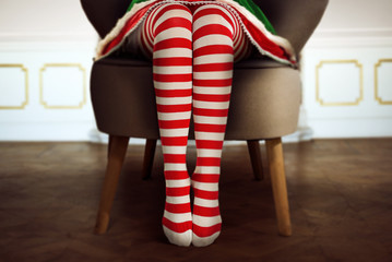 Shapely,long female legs in red and white tights.Girl in a Christmas elf costume is sitting at home and waiting for Christmas presents.December winter time and free space for your text.Copy space.