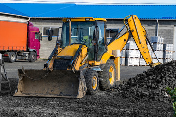 Obraz na płótnie Canvas The yellow all-wheel drive backhoe loader stands on the yard ready for workind on construction site.