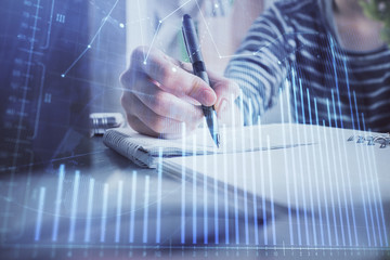 Financial forex graph drawn over hands taking notes background. Concept of research. Double exposure