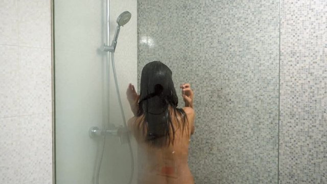 Brunette woman washing hair in the shower. Close-up shot from back. Slow motion. HD