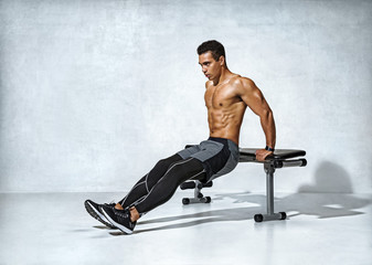 Strong man working out arms muscles doing triceps dips using bench. Photo of latin man with perfect...