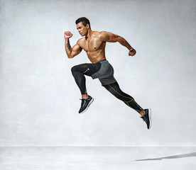 Sporty man jumping. Photo of active man with naked torso on grey background. Dynamic movement. Side...