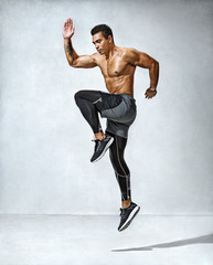Fototapeta na wymiar Sporty man jumping. Photo of active man with naked torso on grey background. Dynamic movement. Side view. Sport and healthy lifestyle