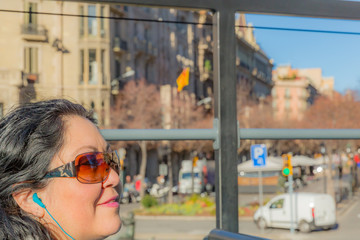 Tourist woman with headphones in the ears listening guide in Barcelona on a tourist bus, sunny day to enjoy the city in Catalonia Spain