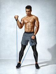 Man performs exercises with expander. Photo of sporty man workout on grey background. Strength and...