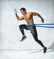 Fototapeta na wymiar Strong man in silhouette using a resistance band. Photo of man performs fitness exercises on grey background. Side view. Full length