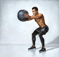 Sporty man doing squats with med ball. Photo of muscular fitness model on grey background. Fitness...