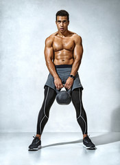 Fototapeta na wymiar Sporty man resting after workout with kettlebell. Photo of athletic man with naked torso and good physique on grey background. Strength and motivation
