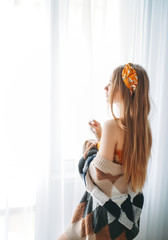 Fototapeta premium Beautiful sensual young woman fair long hair girl wearing in cozy knitted cardigan near window at the home