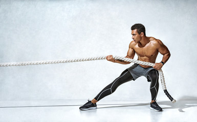 Strong man pulling rope. Photo of sporty man on grey background. Strength and motivation. Side...