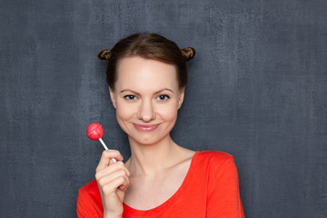 Fototapeta premium Portrait of happy young woman holding pink lollipop in hand