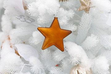 Golden Christmas toy in the form of a star hanging on a white Christmas tree