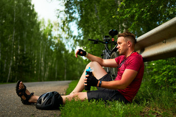 A tired cyclist is sitting on the side of the road. A man with a bicycle is resting.