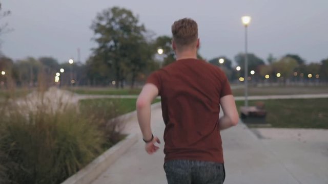Young modern man jogging / exercising in an urban park at night time.