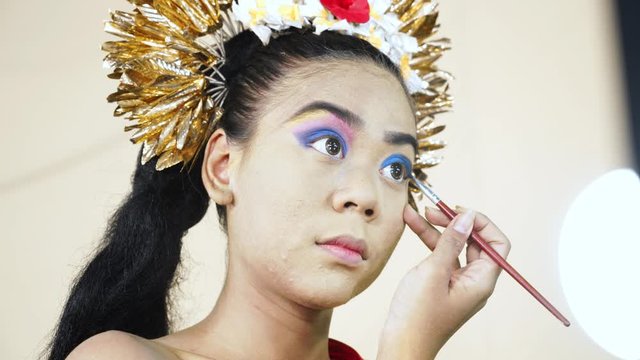 Pretty female balinese dancer coloring her eyelids in makeup room. Shot in 4k resolution