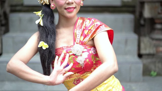 Slow motion of pretty balinese dancer smiling at the camera while showing a welcoming gesture in traditional temple at temple