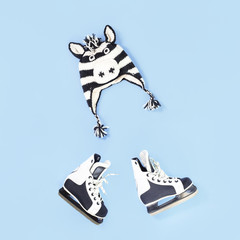 Winter is here creative concept. Zebra funny face winter hat and skates flat lay on baby blue with copy space. Seasonal activity for kids
