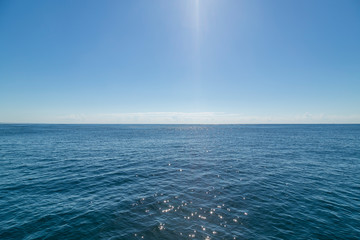 Glaring midday sun creating a beam in the middle of shot giving the calm ocean sparkle