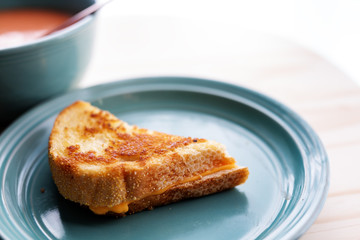 Half of a grilled cheese sandwich on a plate with a bowl of tomato soup. Copy space. 
