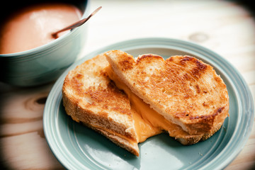 Grilled cheese sandwich on a small plate with a bowl of tomato soup. 