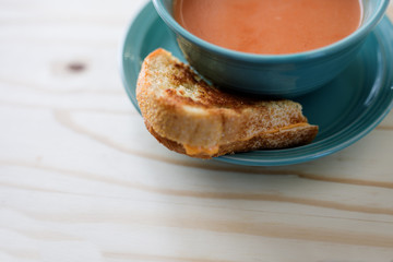 Bowl of tomato bisque soup with half of a grilled cheese sandwich on a plate. 