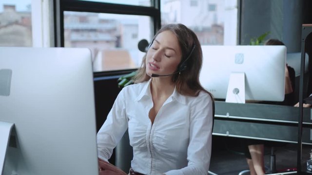 Young woman customer support operator talking with a client discussing business or company services at desktop computer in the office.