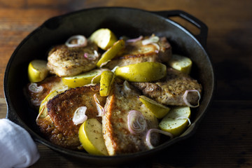 Fried pork chops with apples in a cast iron skillet. 