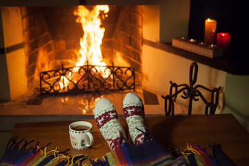 Woman in warm knitted socks in front of a fireplace
