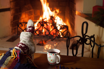 Woman in warm knitted socks in front of a fireplace