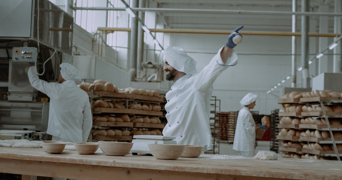 Funny dancing baker in a bakery industry while making the dough for baking a bread he dancing full of energy beside him