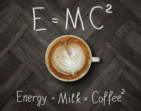 The cup of black energy coffee with milk and two funny formulas. Wooden background.