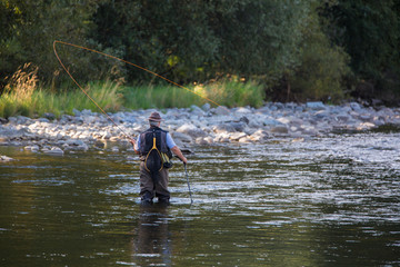 Fly fisherman using flyfishing rod in beautiful river.
