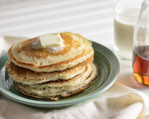 Pat of butter melting on a stack of hotcakes with glass of milk and cloth napkin. 