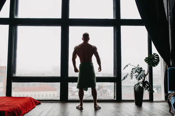 Fototapeta na wymiar silhouette of a sporty sexy bodybuilder man by a large window with a city view.