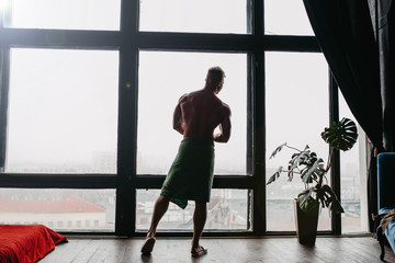 Fototapeta na wymiar silhouette of a sporty sexy bodybuilder man by a large window with a city view.