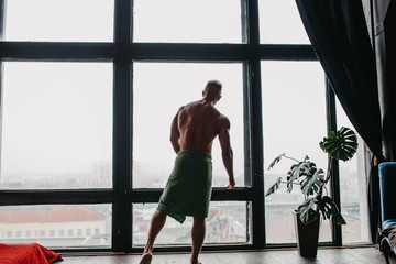 silhouette of a sporty sexy bodybuilder man by a large window with a city view.