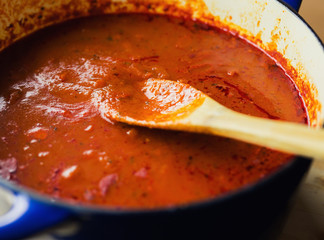 Pot of slow cooked marinara with wooden spoon. 