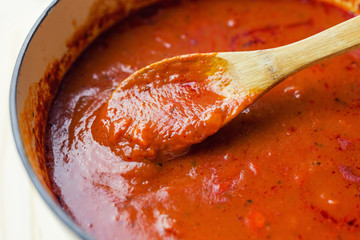 Wooden spoon stirring a pot of marinara sauce. Close up view.  - obrazy, fototapety, plakaty