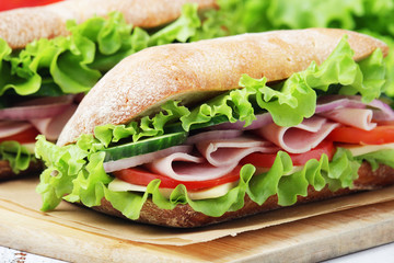 Two sandwiches with fresh vegetables, ham and cheese in ciabatta bread