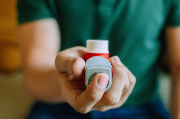A young man is holding an asthma inhaler device while sitting on a couch