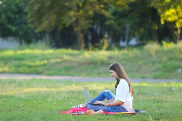 lady sitting in the park and talking on Skype via a laptop with headphones