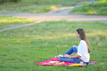 lady sitting in the park and talking on Skype via a laptop with headphones