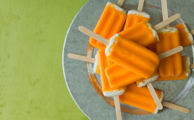 Overhead view of a bunch of orange dreamsicle pops on a serving tray. Top view with copy space, green background. 