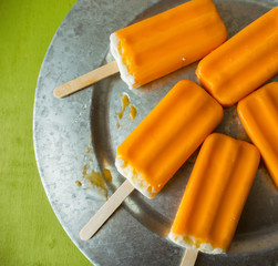 Overhead view of several creamsicles, melting on a galvanized tray. Green background with copy space.
