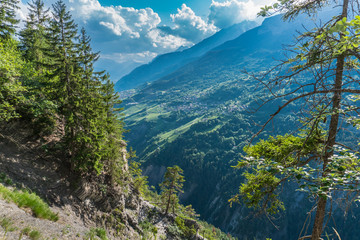 Mountain valley with small villages on the side of the mountain opposite connected by small roads that run between green meadows and forests. The sky covered with clouds.