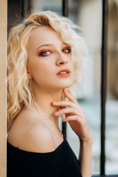 Portrait of pretty blonde woman in black dress poses near wall